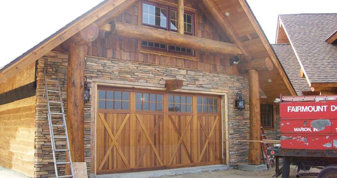 Cedar carriage house garage door on a log and stone home, with a Fairmount Door truck