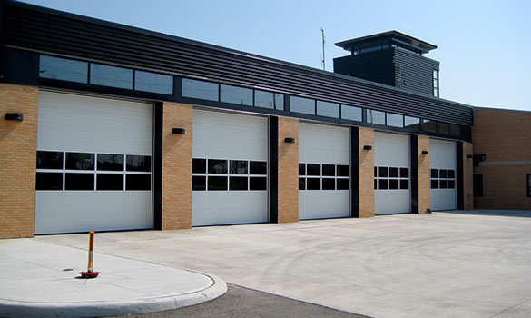 Five white commercial overhead doors with window rows on a brick public building