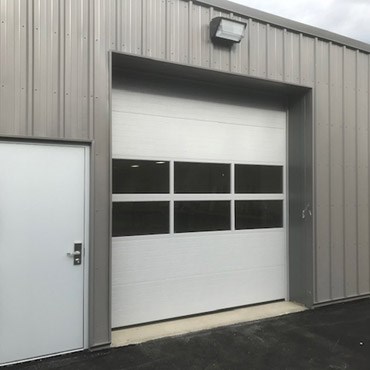 White commercial sectional door with a row of windows on a metal building
