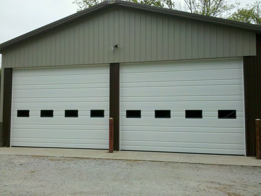 Two white ribbed steel overhead doors with small windows on a pole barn