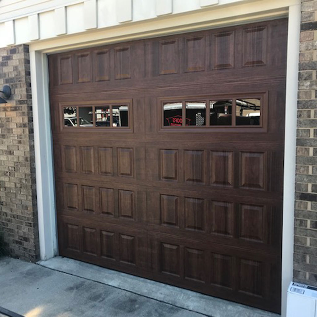 Dark wood-look raised panel garage door with windows on a brick home